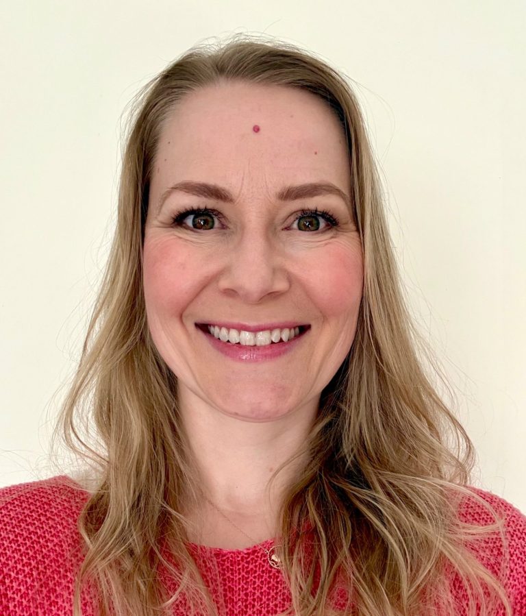 Susi Bukatz • Foto: Privat Lächelnde Frau mit langen, blonden Haaren und pinkem Oberteil vor neutralem Hintergrund.